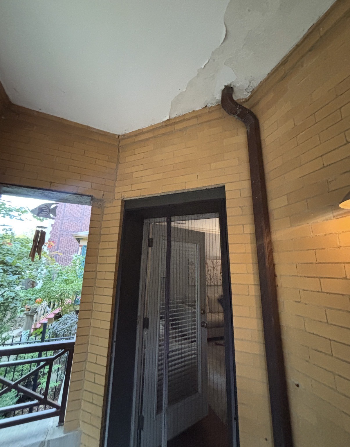Porch ceiling water damage before, and the new exterior downspout after a gutter re-route at a Lake View condo complex (Before)